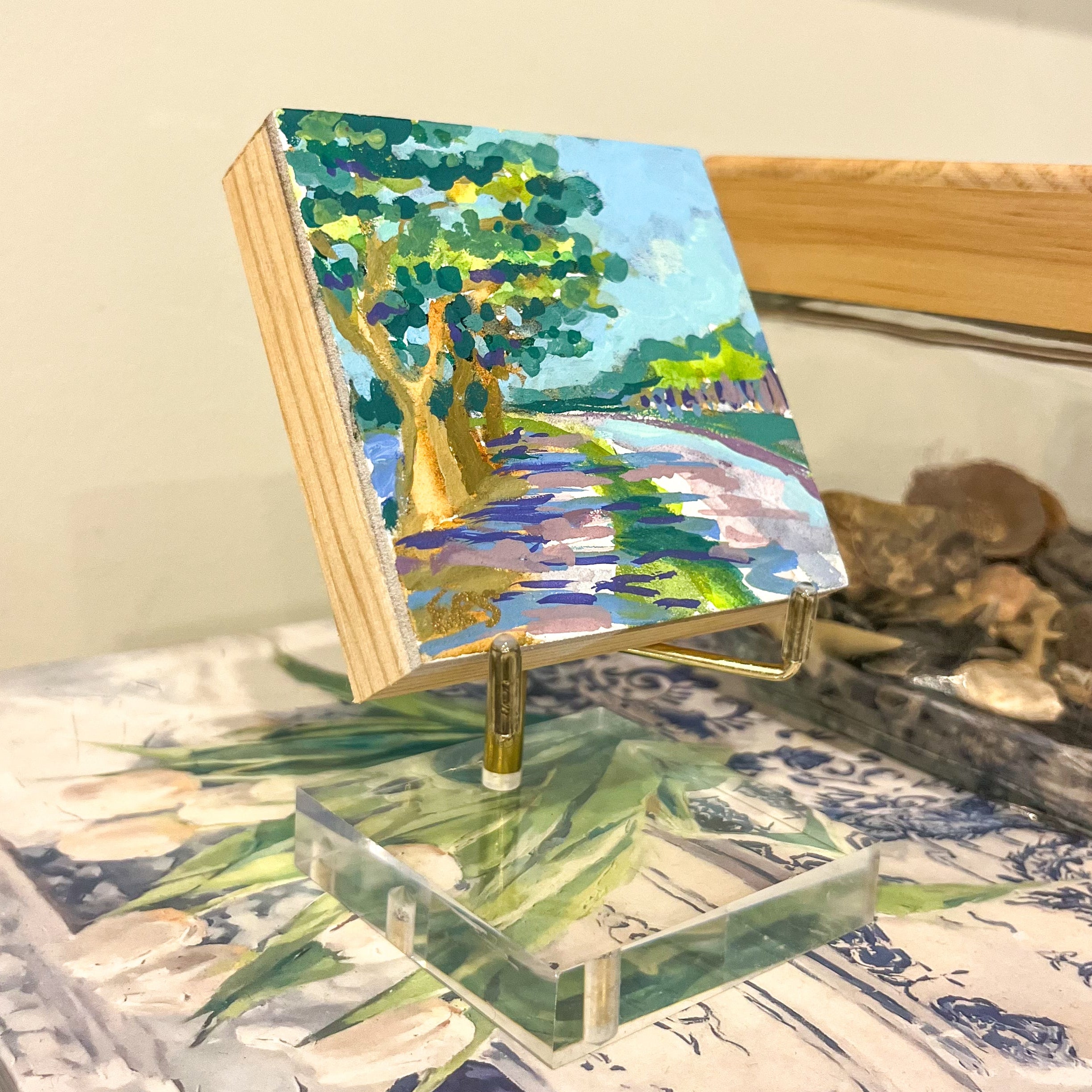 Small landscape painting on an easel with a palette and brushes in the background