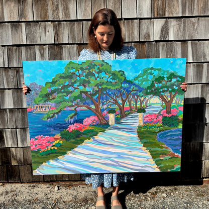 Elizabeth Sheats holding a colorful painting of a garden path against a wooden wall.