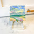 Small abstract painting on a stand with a marble surface and wooden object in the background
